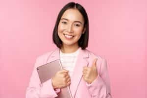 girl in office in business suit, holding digital tablet, showing thumbs up.