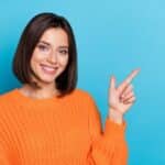 A cheerful girl in bright orange knitted sweater demonstrating a empty hand copy space sign