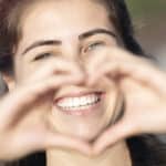 A woman smiling and making a heart with her hands after getting porcelain veneers in Sugar Land