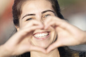 A woman smiling and making a heart with her hands after getting porcelain veneers in Sugar Land